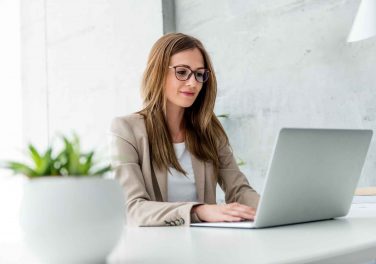 AdobeStock_148435018 woman with glasses sitting at desk using laptop