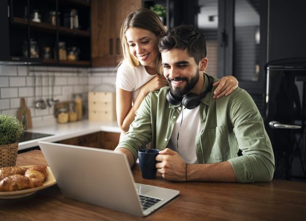 Portrait of a happy young couple smiling in the morning, using laptop in a modern kitchen